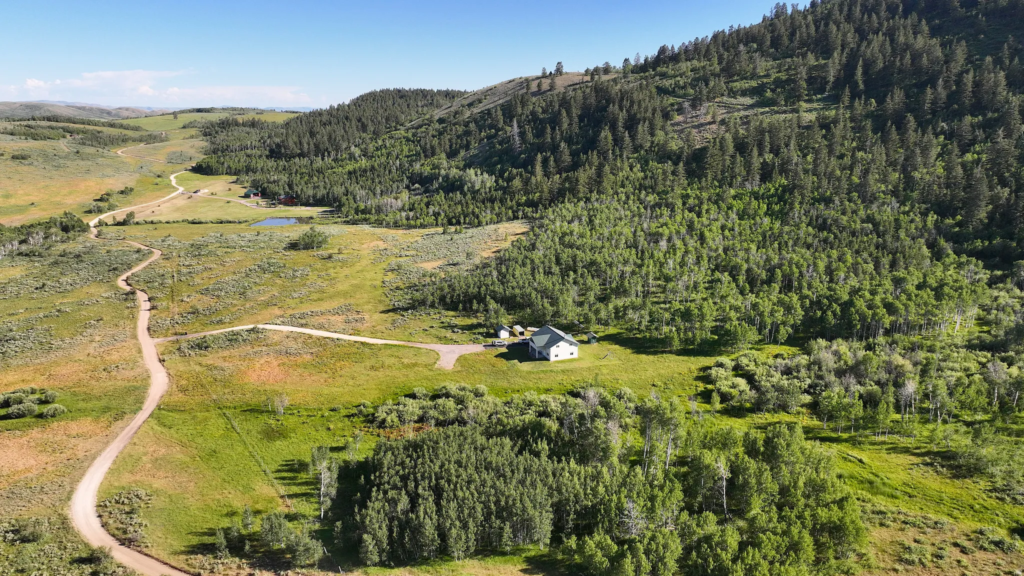 Expansive natural landscape featuring a single-story residence, surrounded by mature trees and verdant hillsides
