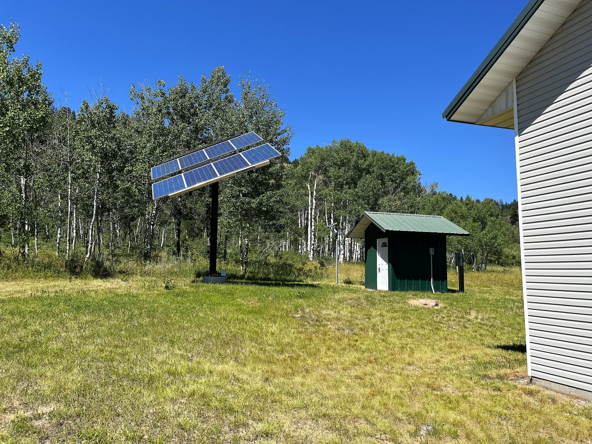 Solar panel array featuring a ground-mounted system and a nearby utility structure with a pitched metal roof