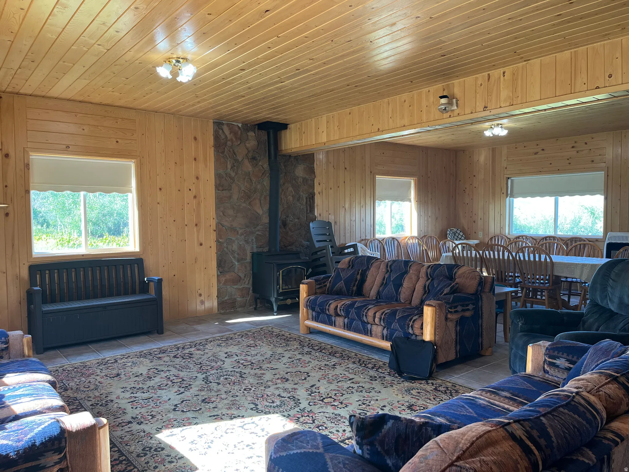 Spacious interior featuring wood-paneled walls and ceiling, a stone-faced accent wall, and a built-in wood-burning stove