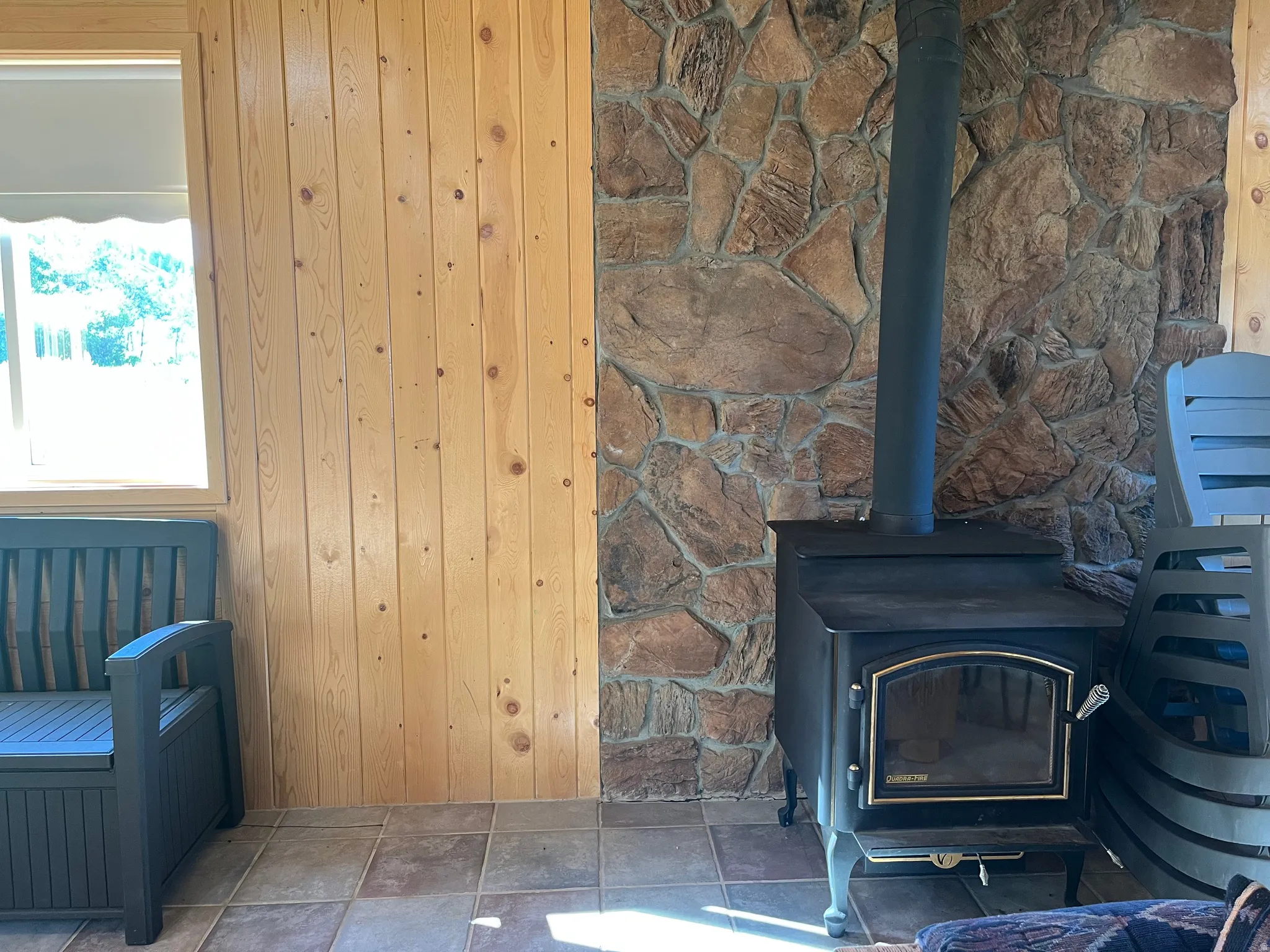 Freestanding wood stove with a glass door and brass accents, set against a stone-clad wall