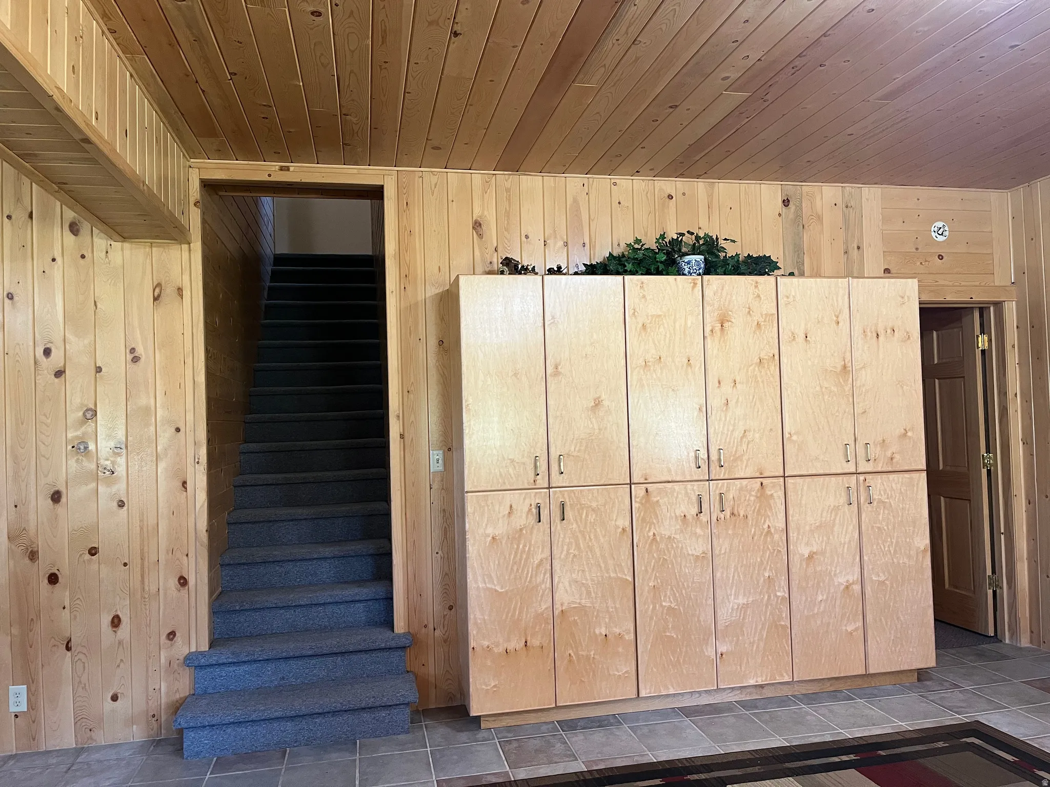 Wood-paneled room featuring extensive built-in cabinetry, a carpeted staircase, and tiled flooring