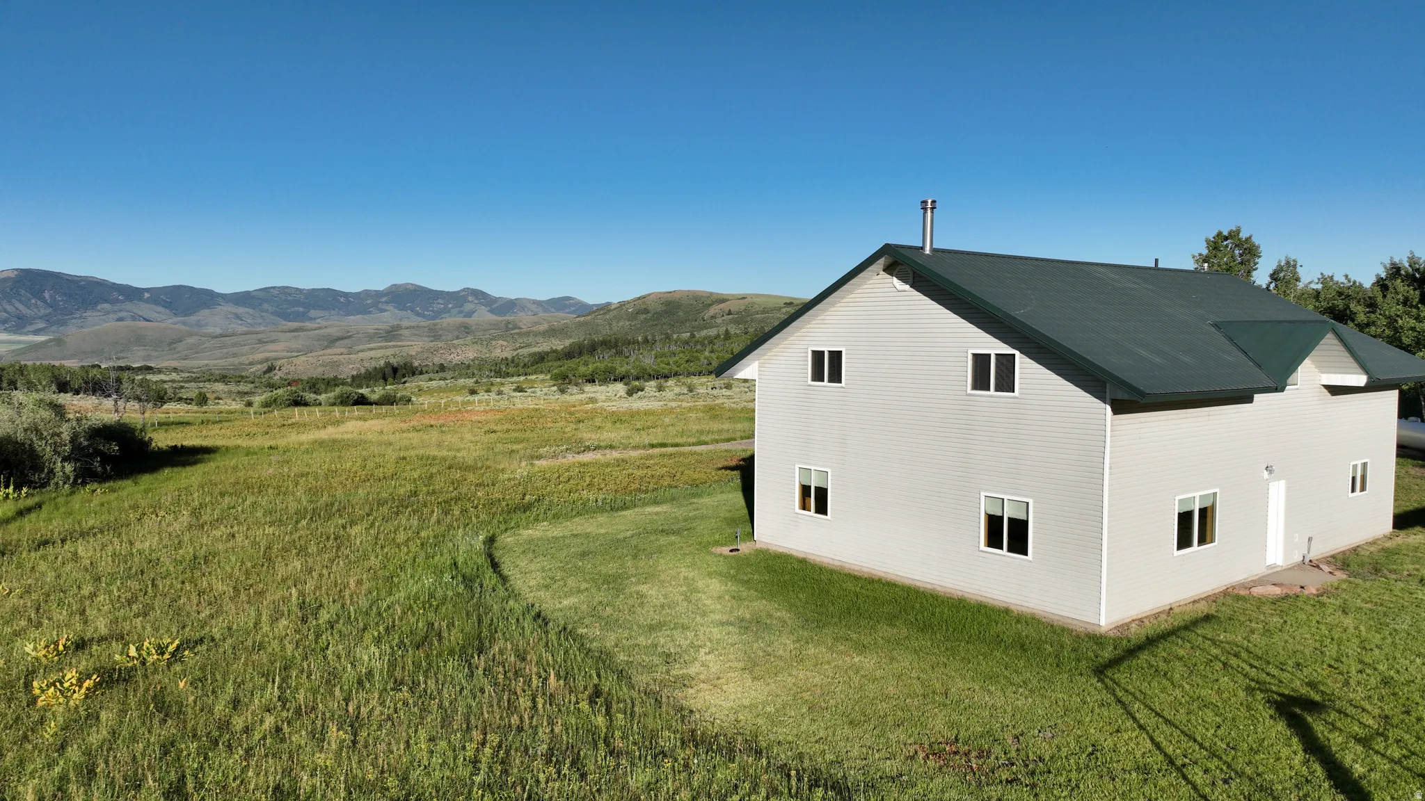 Light gray siding exterior with a dark green roof, featuring multiple windows and a mountain backdrop