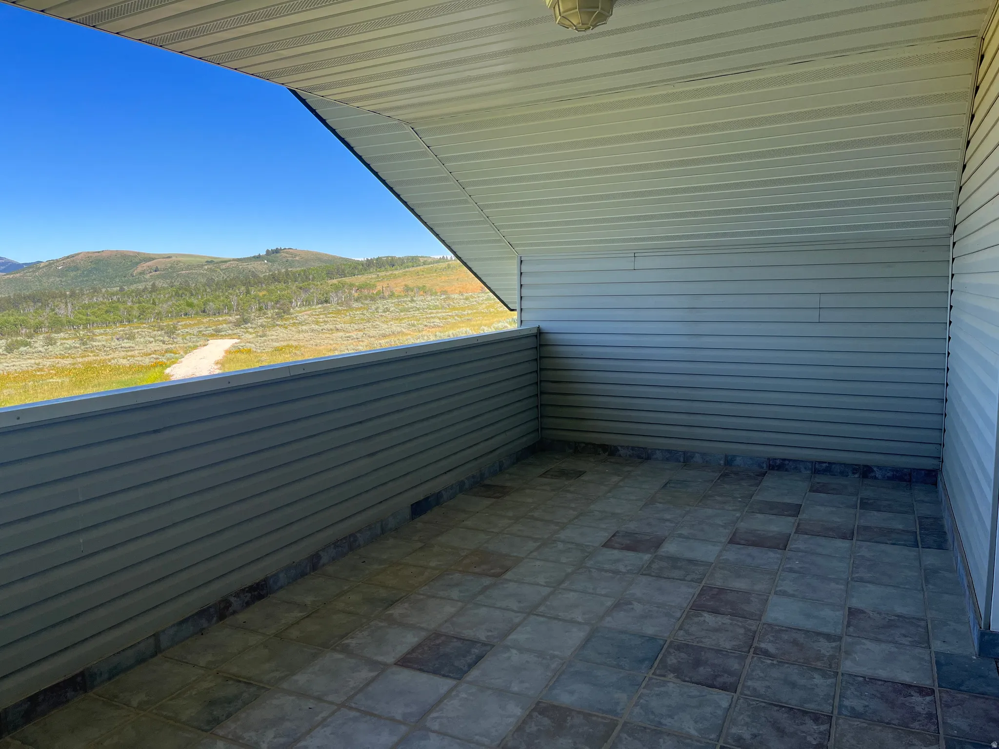 Covered patio area with tiled flooring, horizontal paneling, and an exposed ceiling light fixture