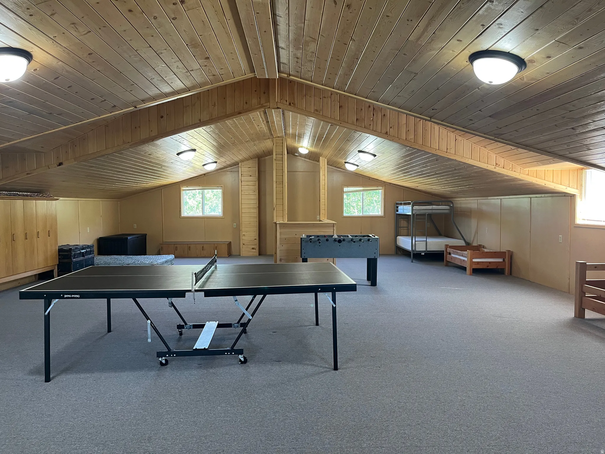 Spacious room featuring sloped wood-paneled ceilings, wall-to-wall carpeting, multiple windows providing natural light, recessed lighting, and extensive built-in cabinetry