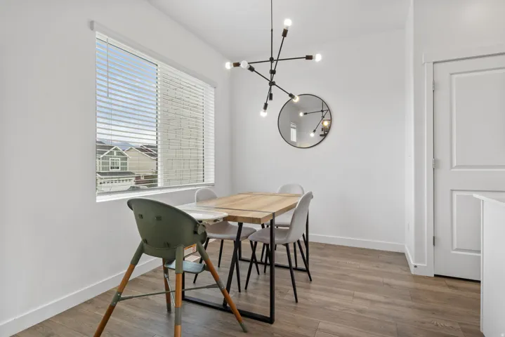Spacious dining area featuring wood-finish flooring, a contemporary black chandelier, and a round wall mirror