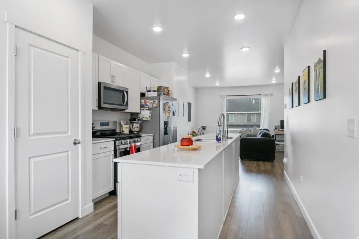 Modern kitchen featuring white cabinetry, stainless steel appliances, a white island with an undermount sink, recessed lighting, and wood-finish flooring