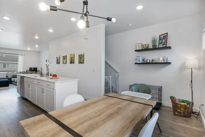 Open-concept kitchen and dining area featuring a spacious island with a stainless steel dishwasher, light wood-finish flooring, recessed lighting, and a contemporary linear chandelier