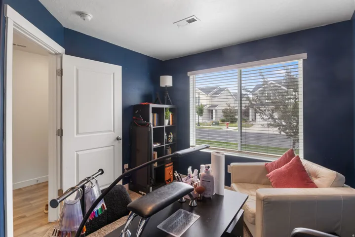 Room with dark blue walls, light-toned wood-finish flooring, and a large window with horizontal blinds