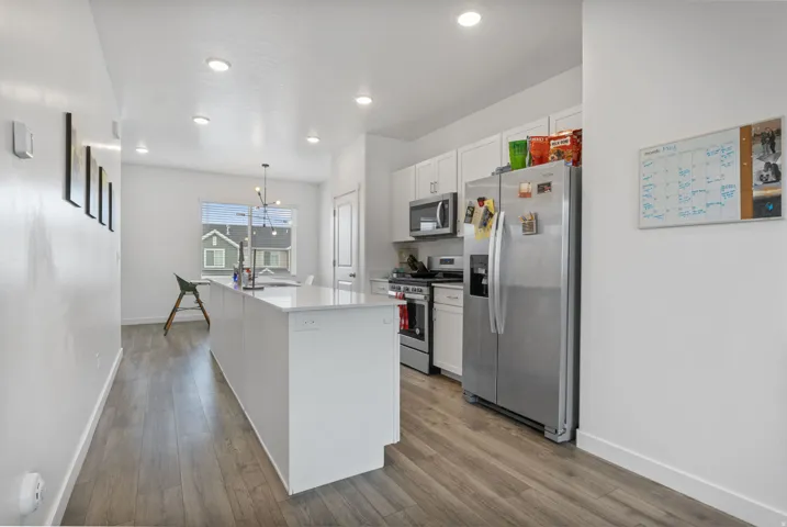Kitchen featuring an expansive island with a light-toned countertop, wood-finish flooring, recessed lighting, white cabinetry, and stainless steel appliances