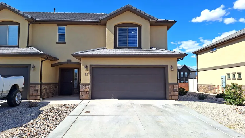 Stucco exterior featuring stone accents, a two-car garage, and a covered entry