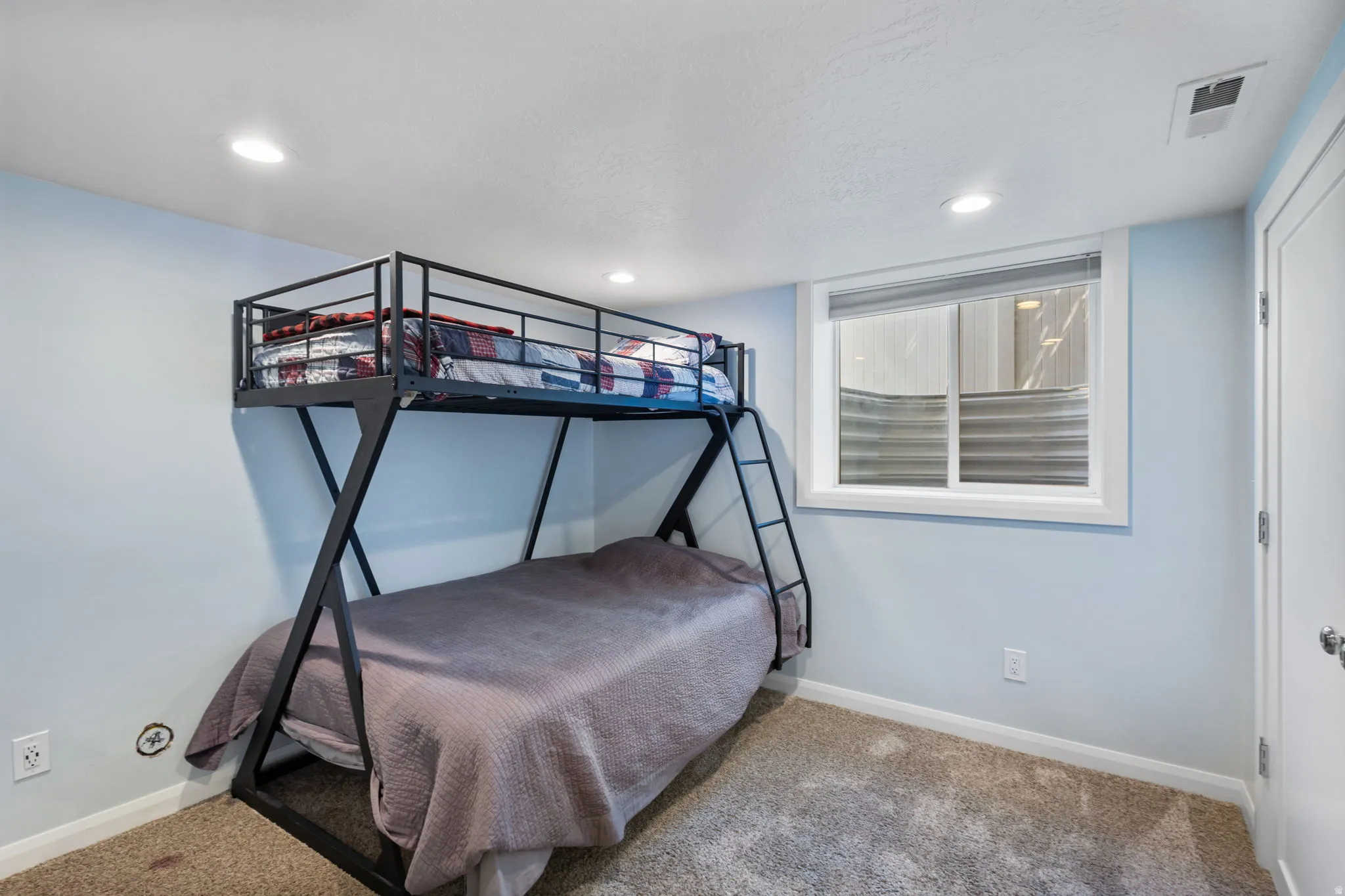 Bedroom 2 Carpeted room with light blue painted walls, a sliding window with horizontal blinds, recessed ceiling lighting, and a white interior door