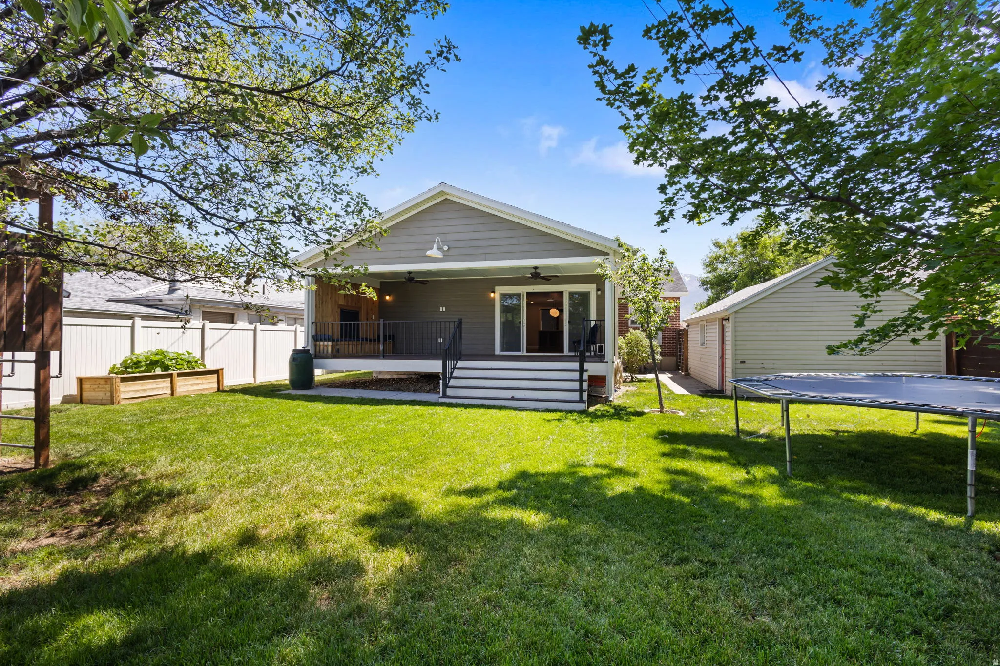 Expansive green lawn with a covered porch featuring ceiling fans, a white privacy fence, and a detached structure