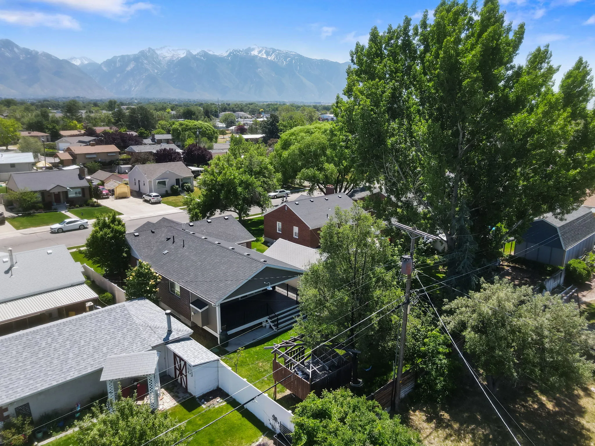 Aerial perspective showcasing a covered deck, mature trees, and a spacious green lawn