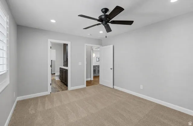 Primary bedroom with attached bathroom and closet. Carpeted interior space with light grey walls, recessed lighting, and a dark-toned ceiling fan