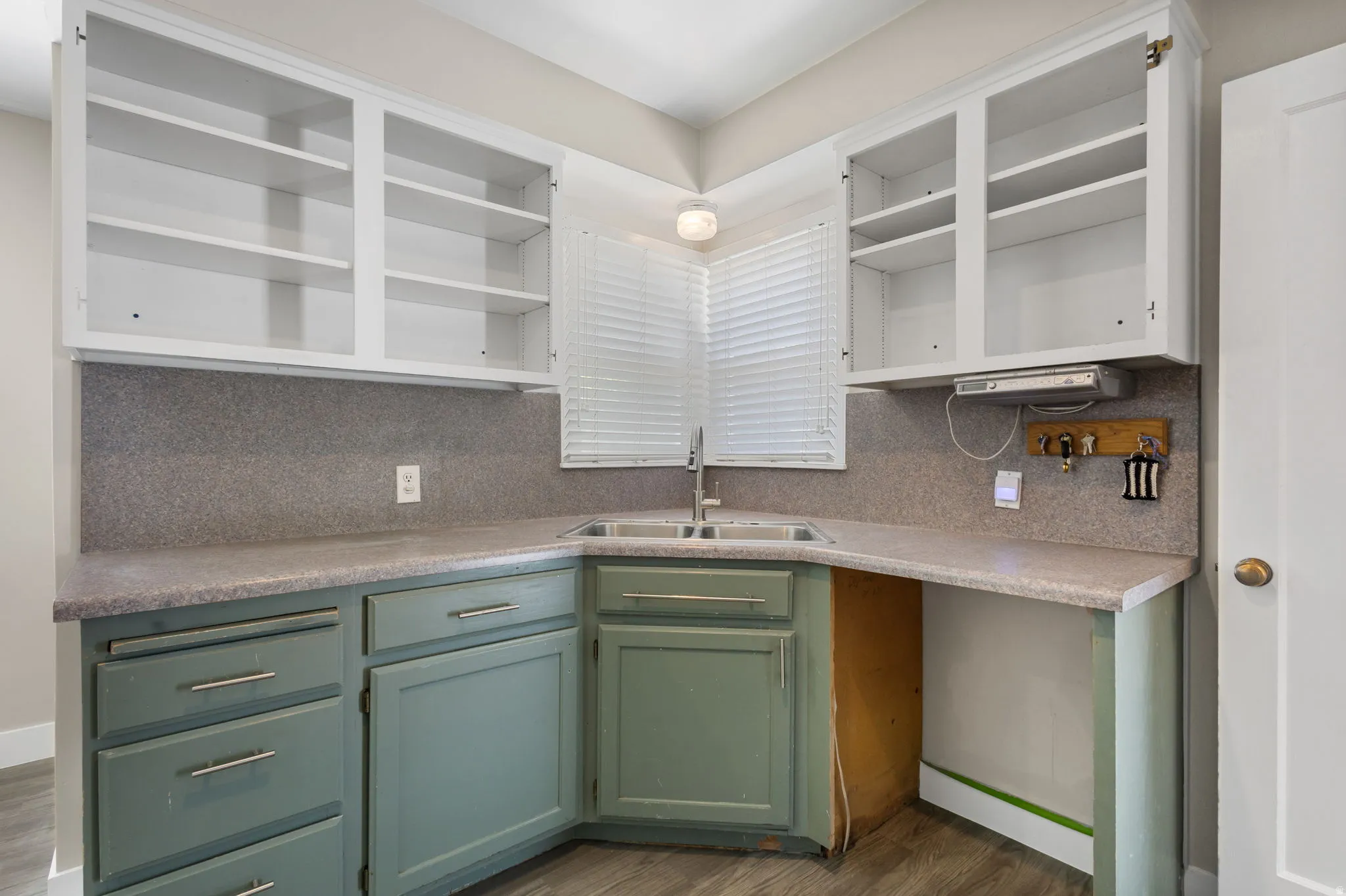 Efficient kitchen corner featuring a double basin sink, white upper cabinetry, and contrasting green lower cabinetry with silver hardware