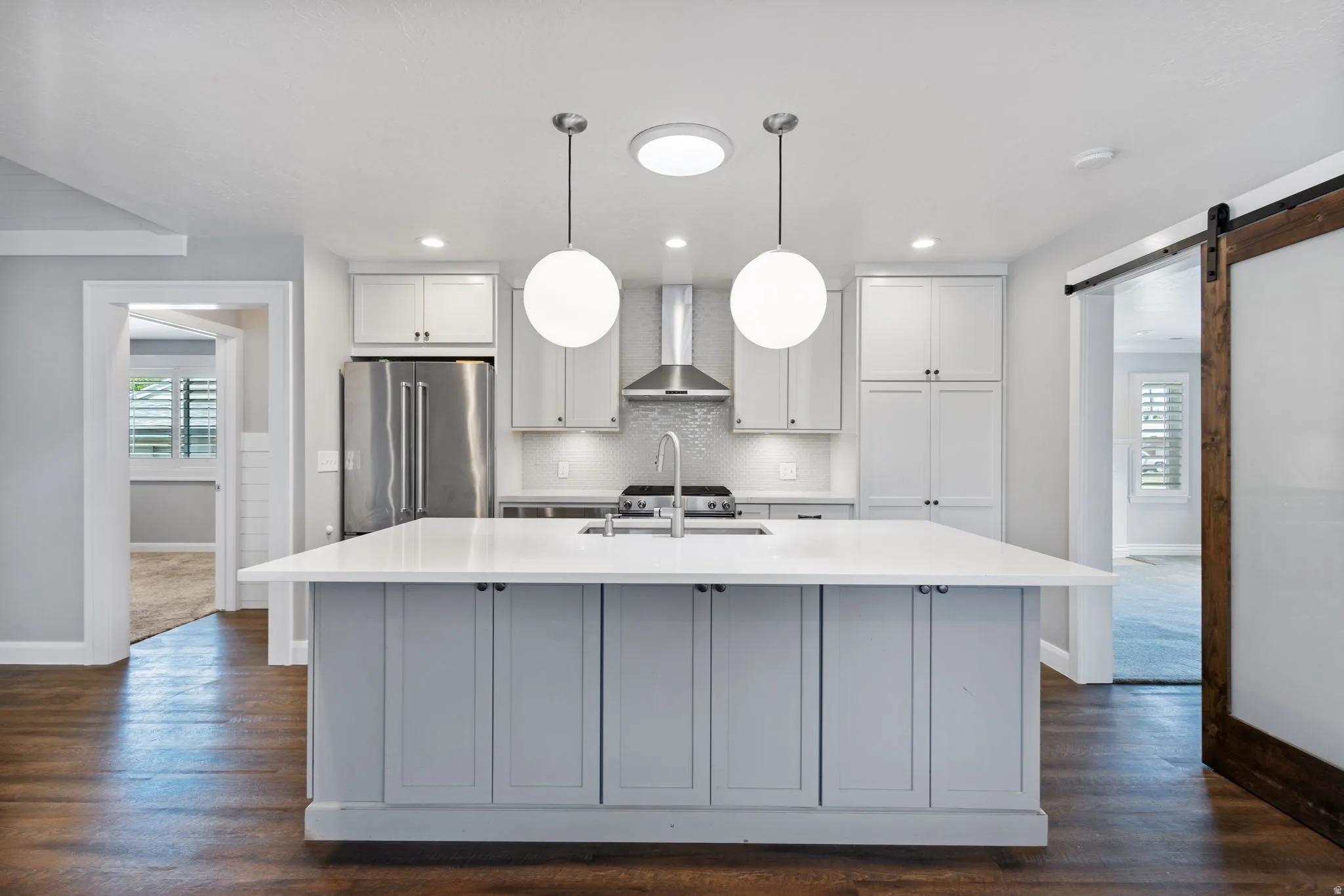 Modern kitchen featuring a light gray island with a white countertop, two pendant lights, stainless steel appliances, and wood-finish flooring