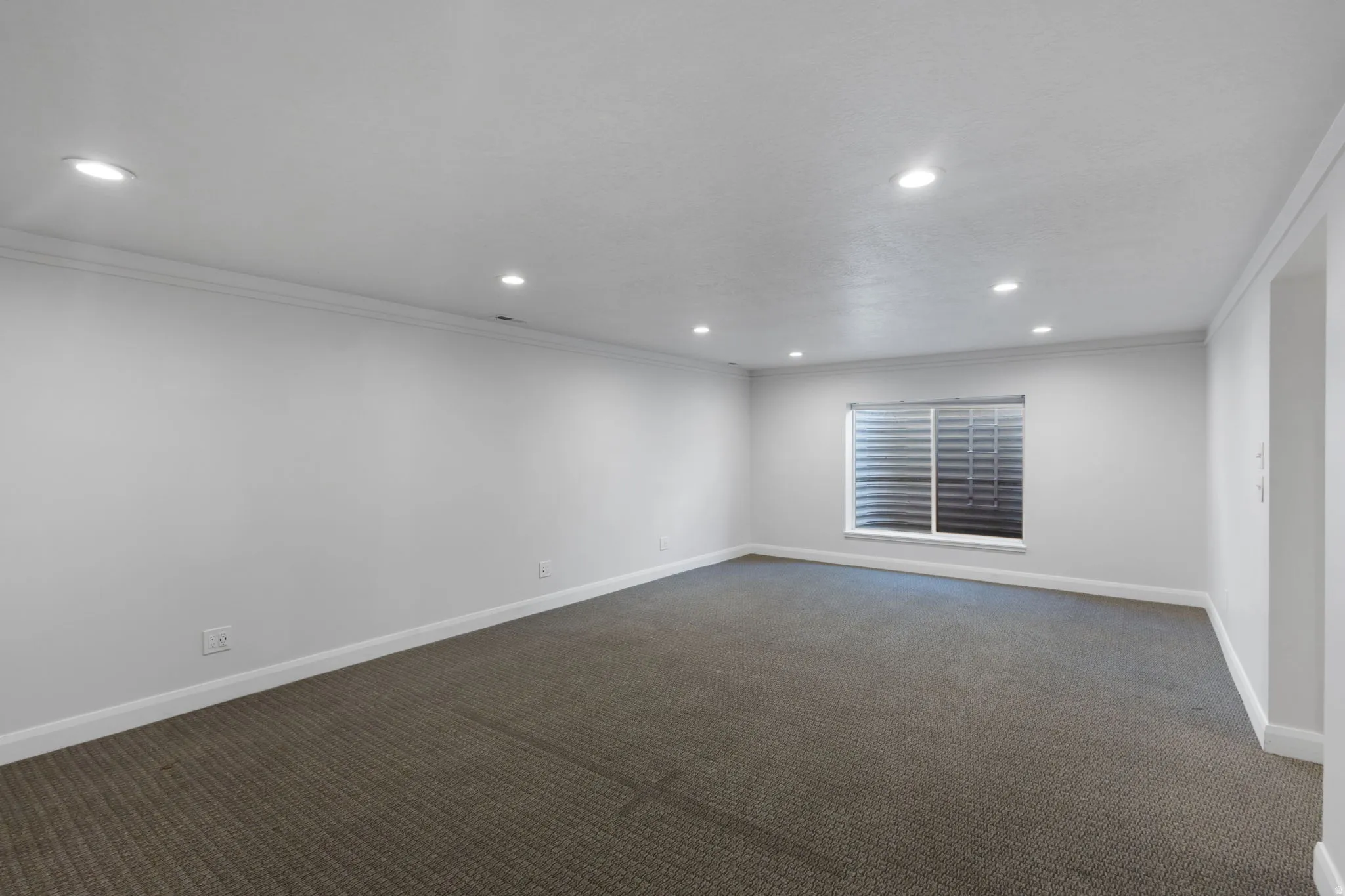 Spacious room featuring neutral carpeting, white baseboards, and bright white walls