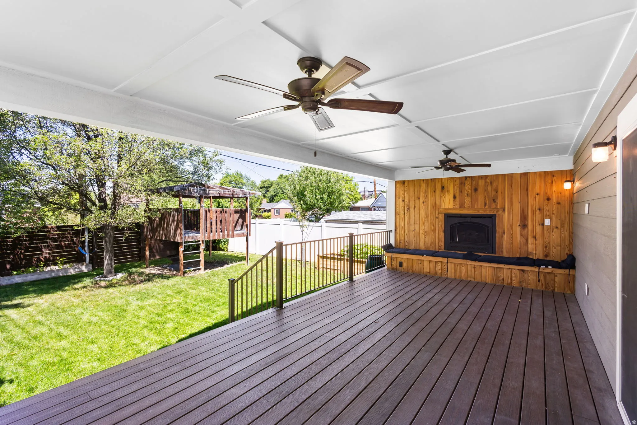 Spacious covered deck featuring a fireplace, built-in bench seating, wood-finish flooring, and multiple ceiling fans