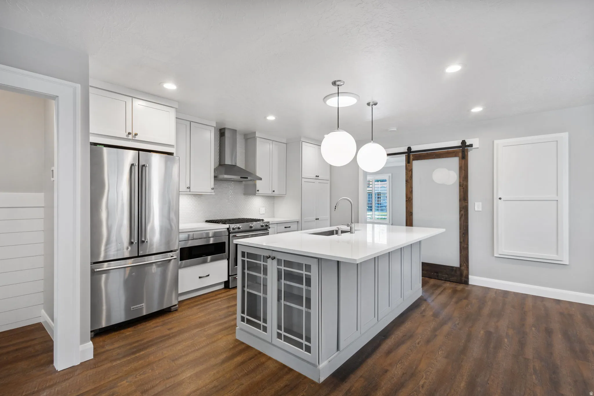 Contemporary kitchen featuring a light gray island with integrated sink, white perimeter cabinetry, and stainless steel appliances