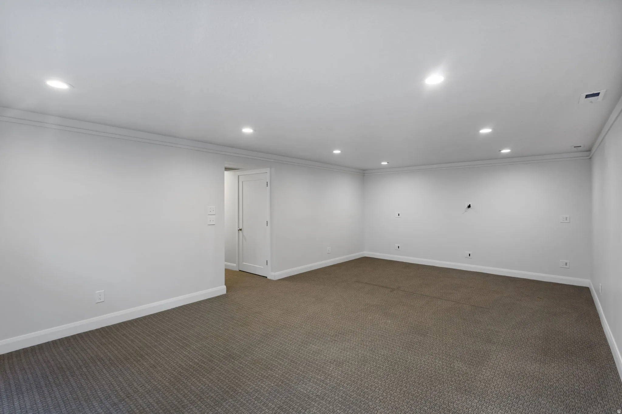 Spacious room featuring neutral carpeting, recessed lighting, white walls, and crown molding