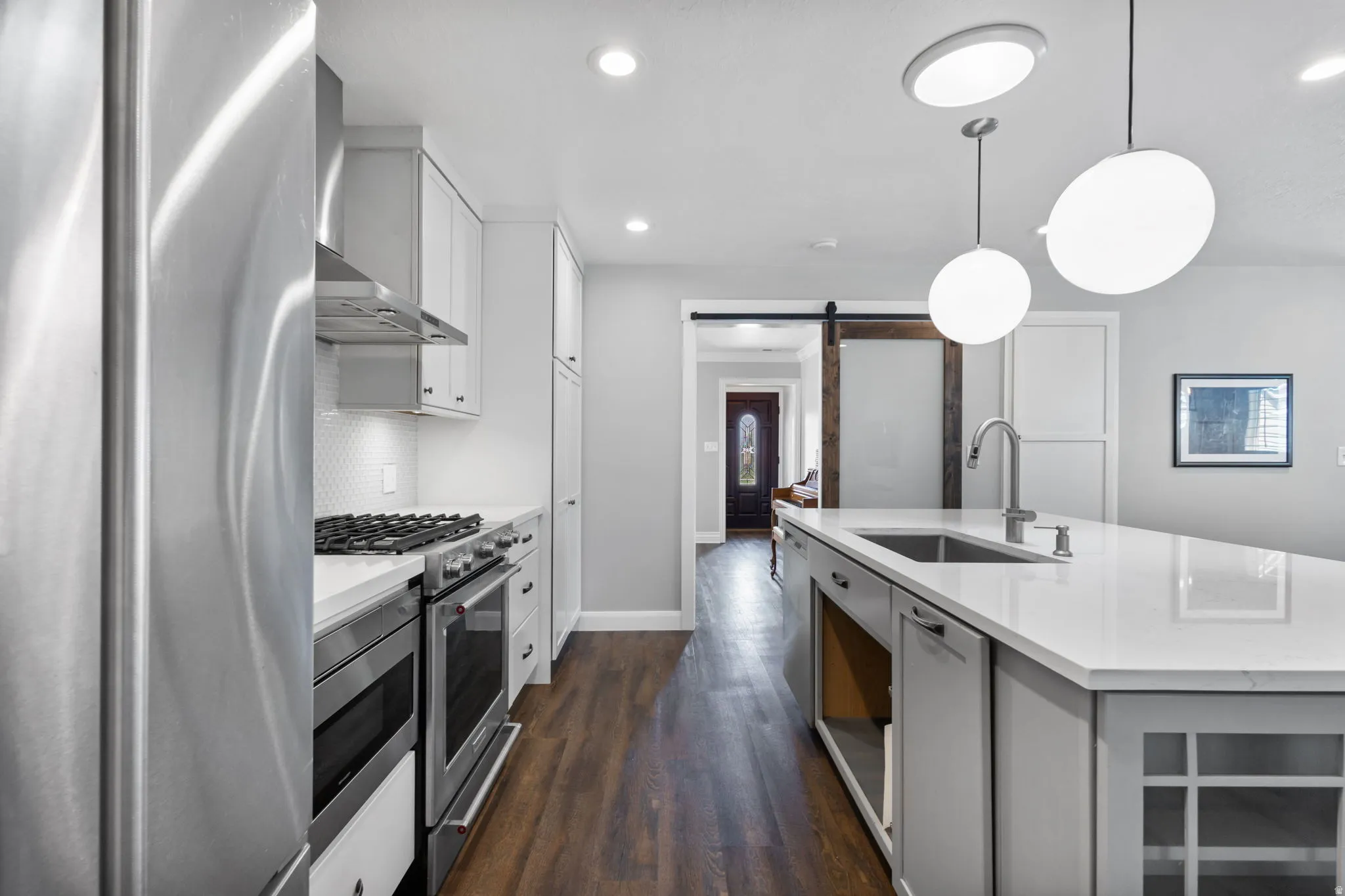 Kitchen featuring wood-finish flooring, white cabinetry, integrated stainless steel appliances, and a central island with an undermount sink and pendant lighting