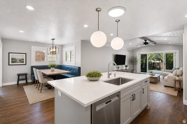 Kitchen island with integrated sink and dishwasher, featuring pendant lighting, wood-finish flooring, and a built-in dining nook