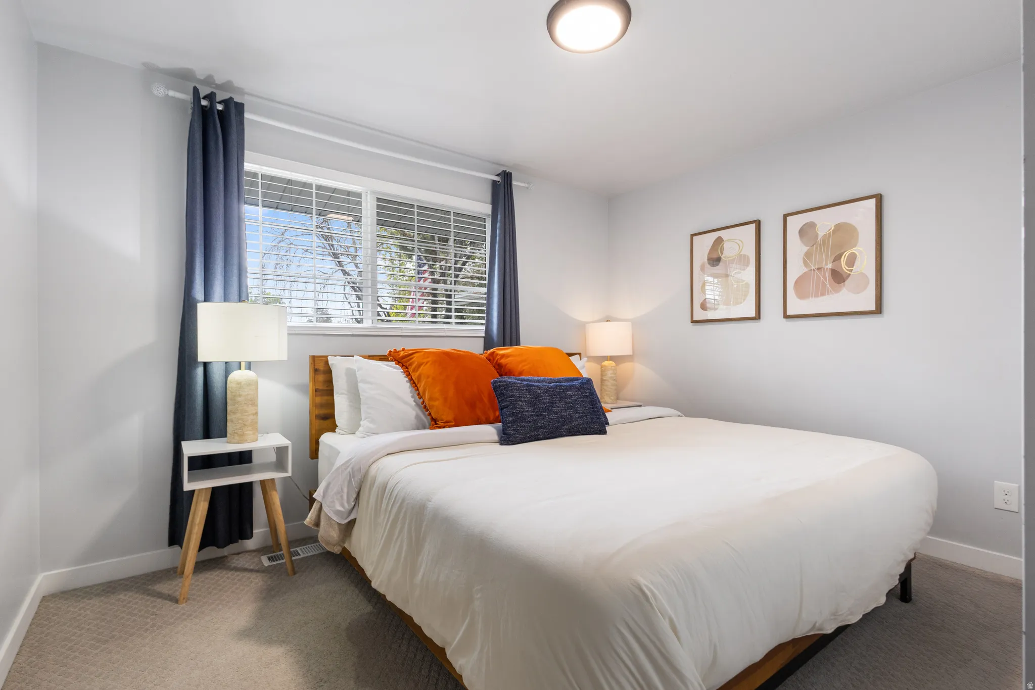 Bright bedroom featuring a large window with white blinds, neutral carpeting, and light gray walls