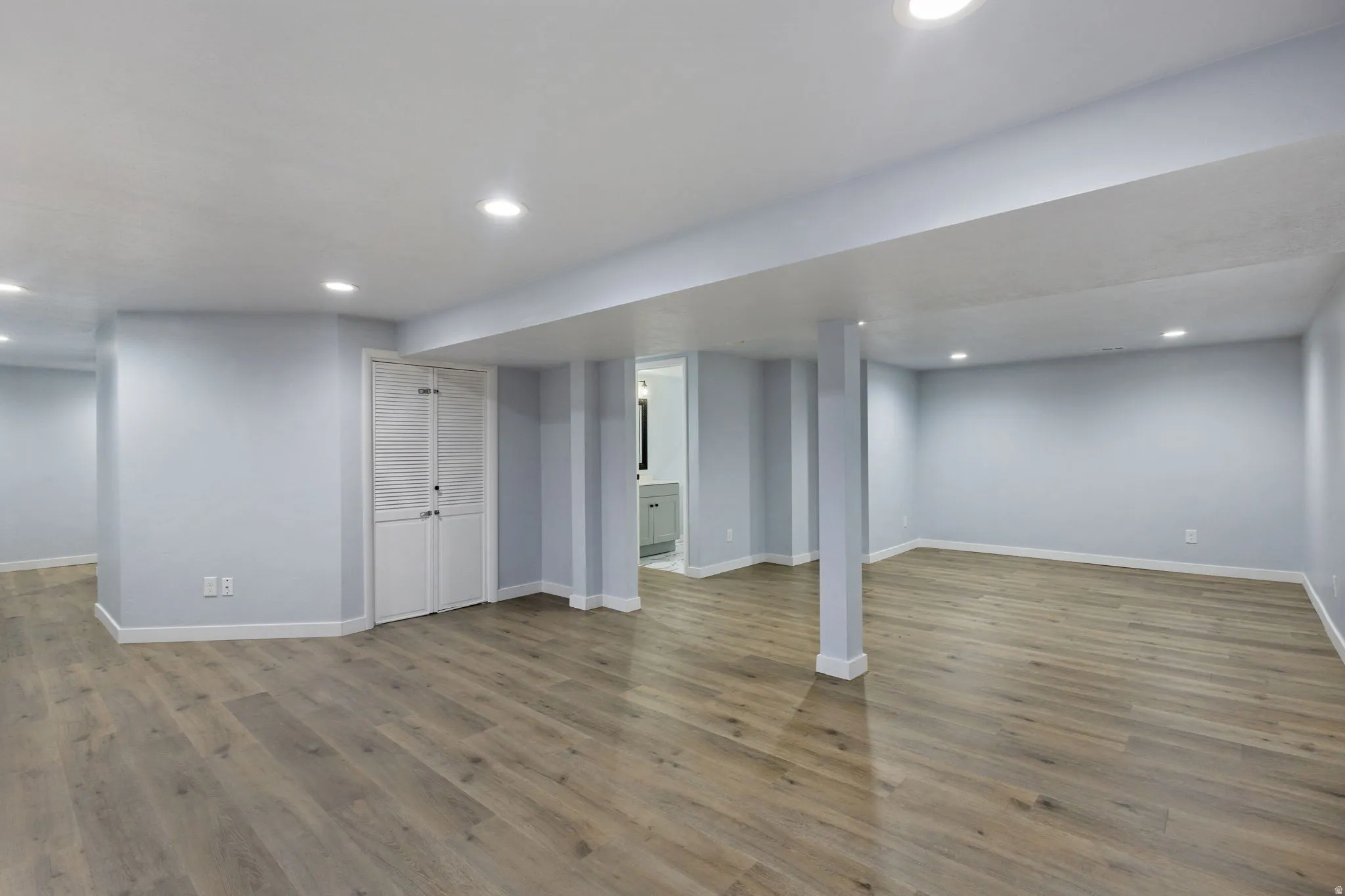 Spacious interior with wood-finish flooring, recessed lighting, light blue walls, and white baseboards