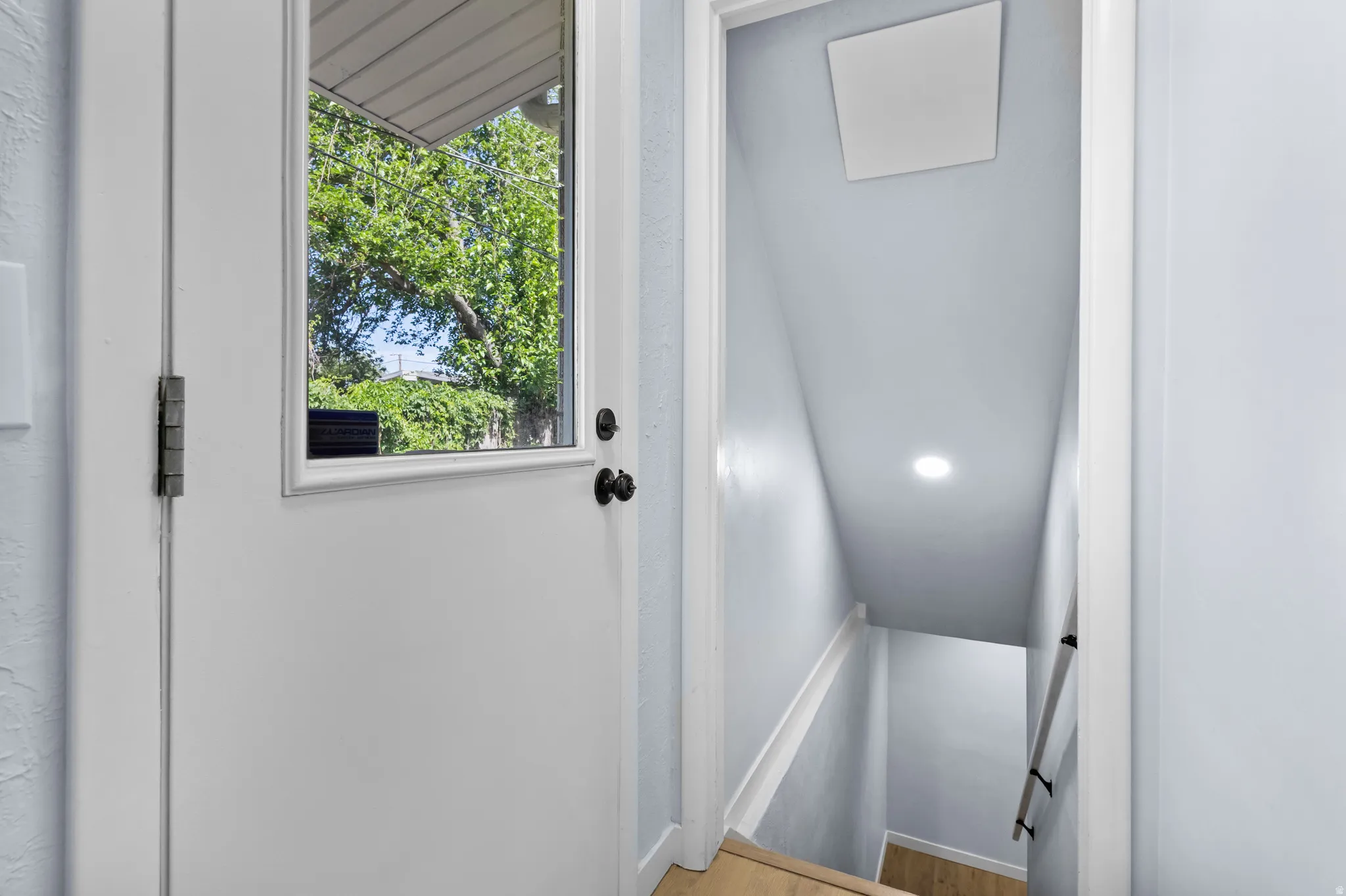 White door with an integrated window featuring dark hardware, light gray walls, wood-finish flooring, recessed lighting, and a white access panel