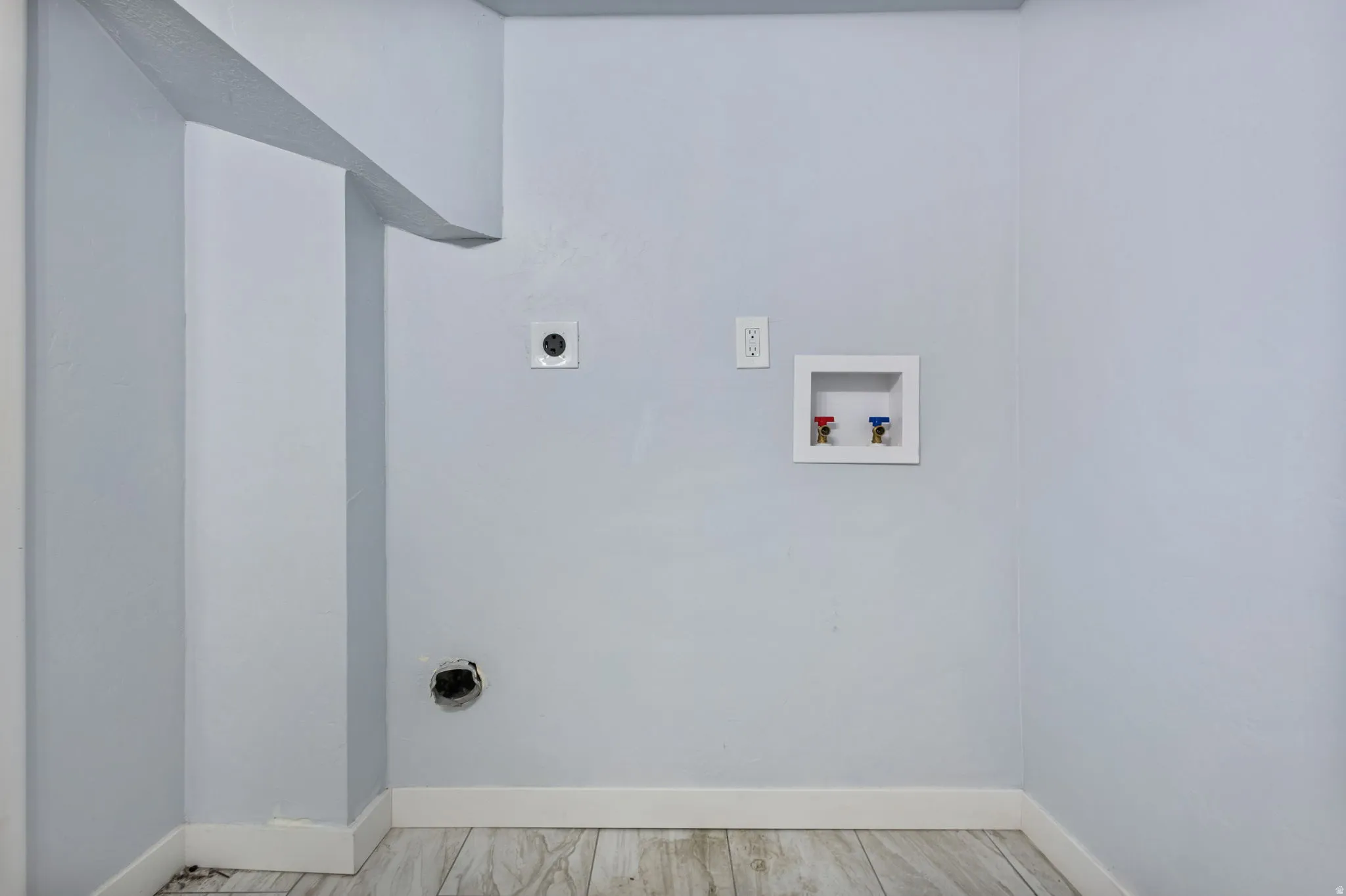 Laundry area with wood-finish flooring, light blue walls, baseboard trim, washer/dryer hookups, and an electrical outlet
