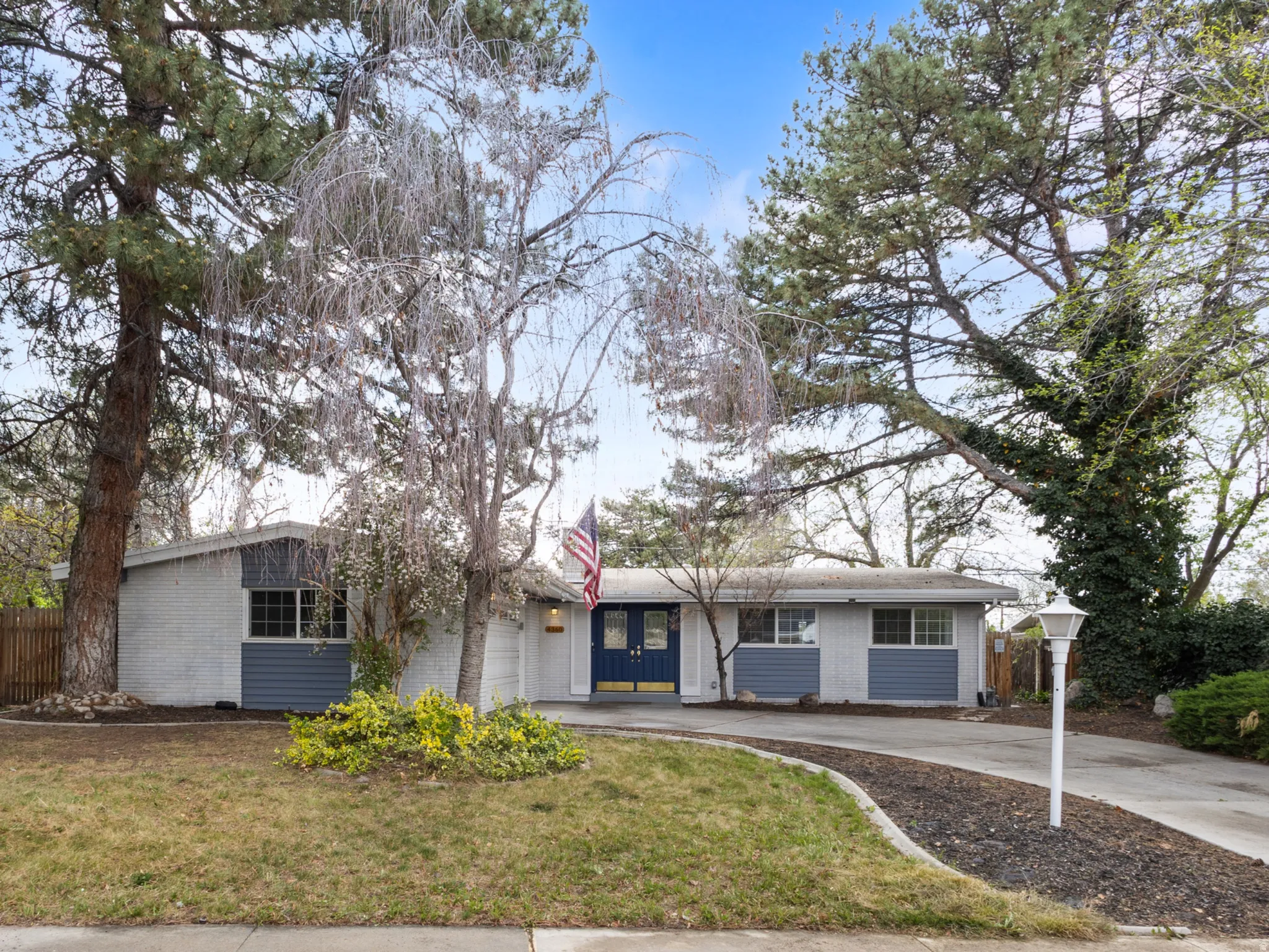 Ranch-style residence featuring a gray and blue exterior, a concrete driveway, and mature trees