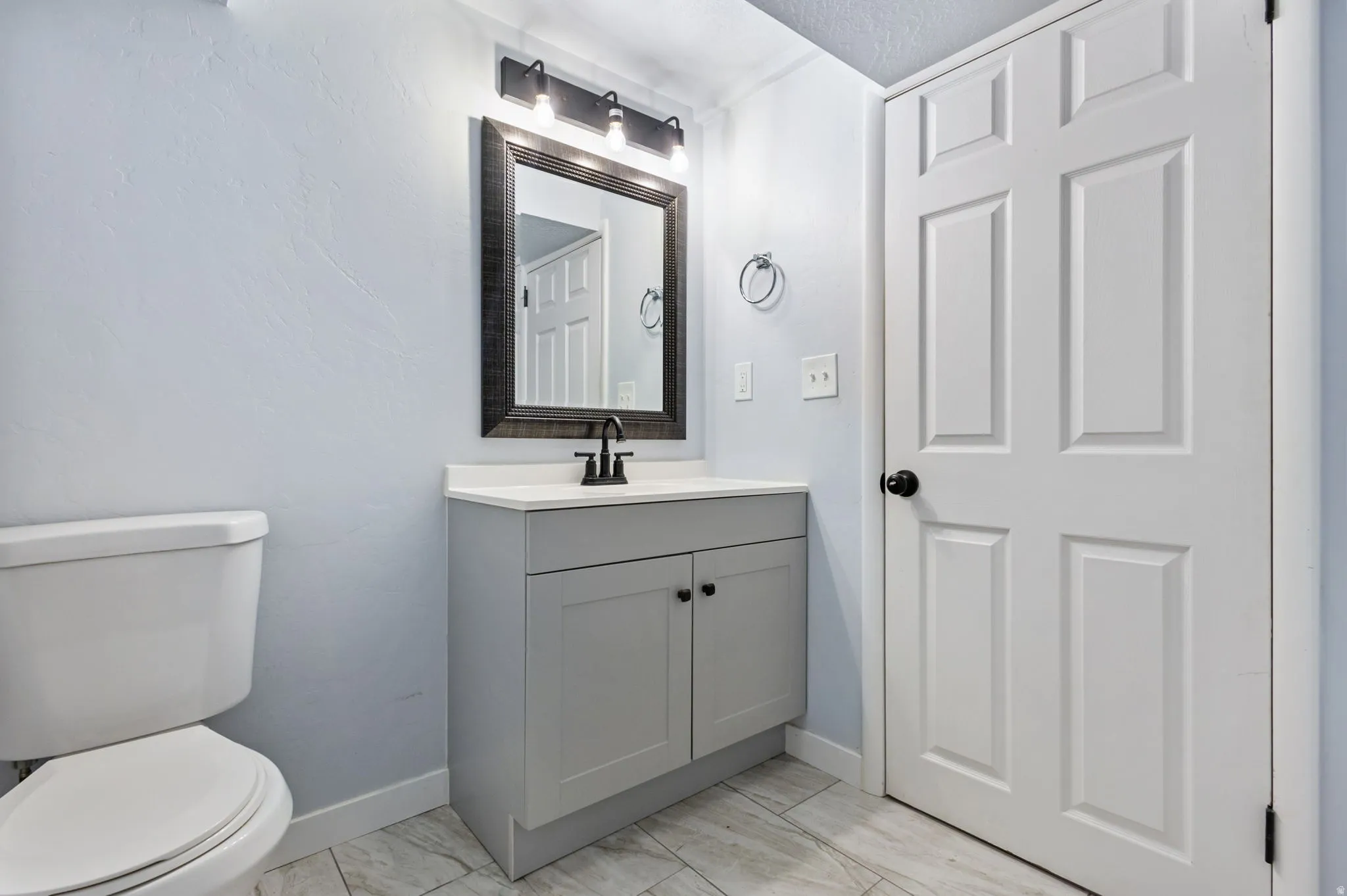 Bathroom vanity featuring a light gray cabinet, white countertop, and black faucet