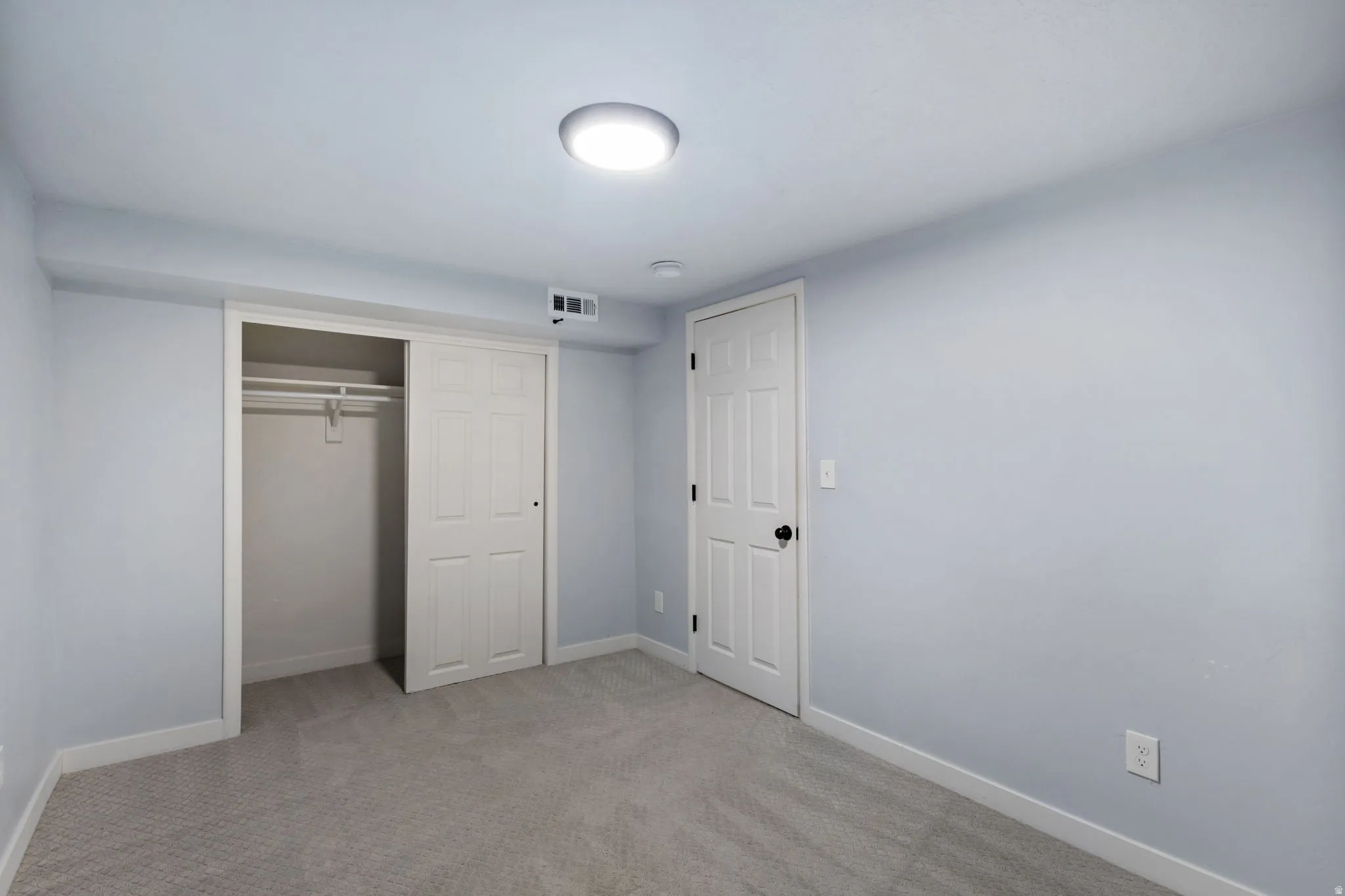 Neutral-toned room featuring a flush-mount ceiling light fixture, light gray walls, and textured gray carpeting