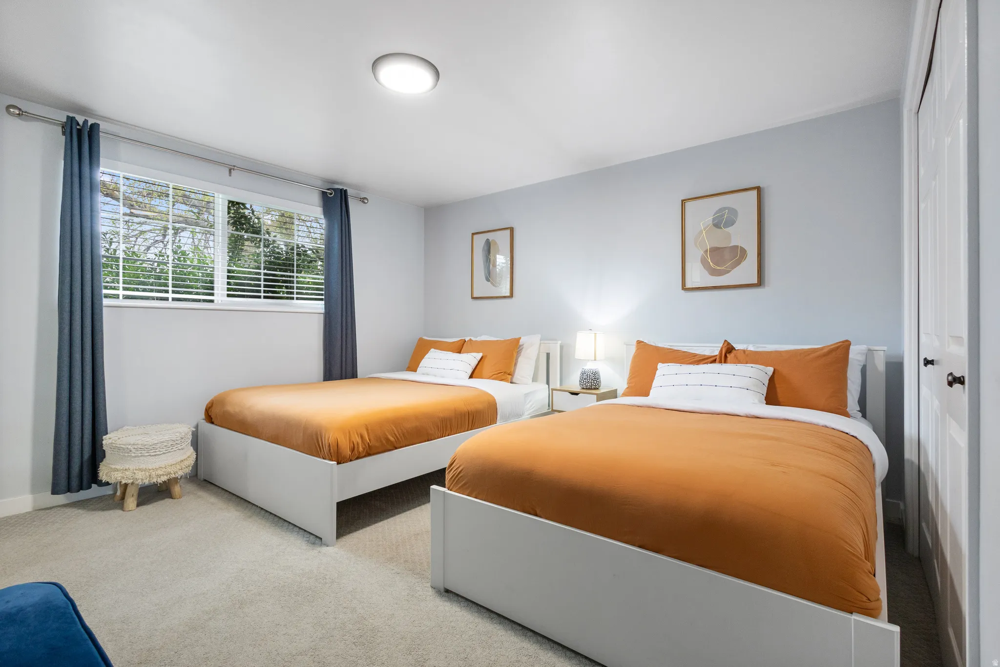 Light-filled room featuring two beds, soft carpet flooring, a window with blinds, and a built-in closet with white bifold doors