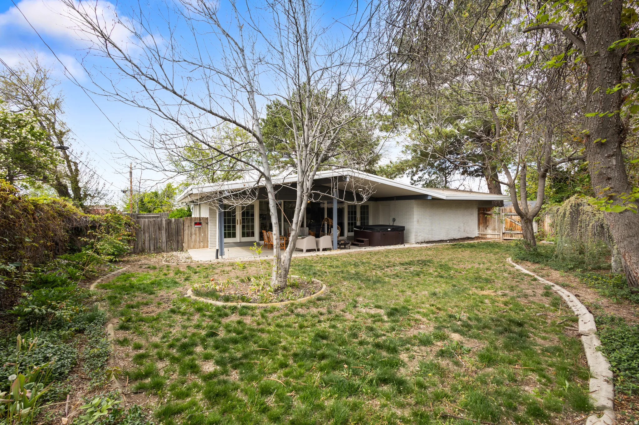 Expansive backyard featuring a covered patio, a built-in spa, a large lawn area, mature trees, and a wooden perimeter fence