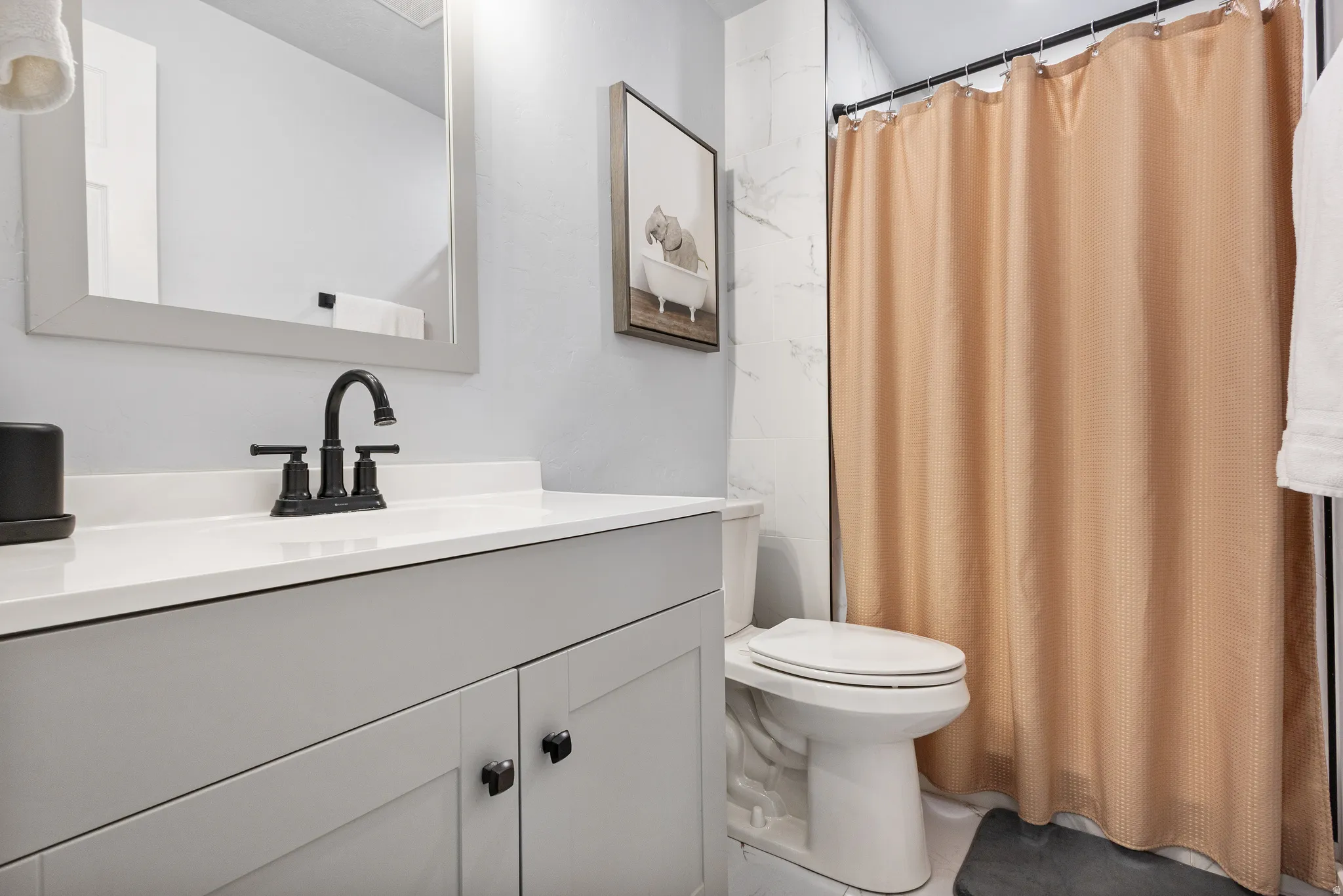 Bathroom featuring a vanity with a white countertop and matte black faucet, framed mirror, and a shower with white tile surround