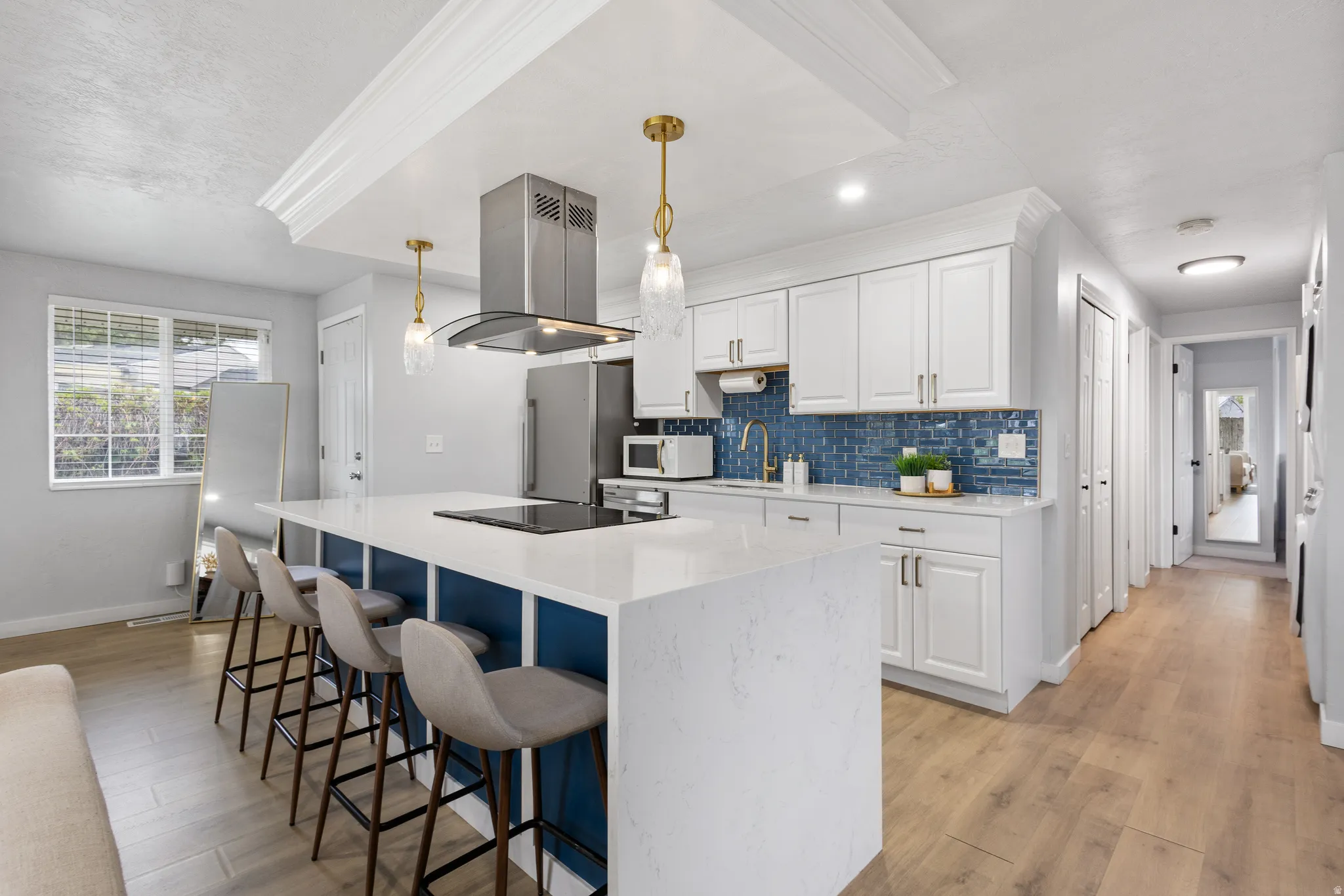 Gourmet kitchen featuring a large central island with integrated cooktop, white shaker cabinetry, blue tile backsplash, and wood-finish flooring