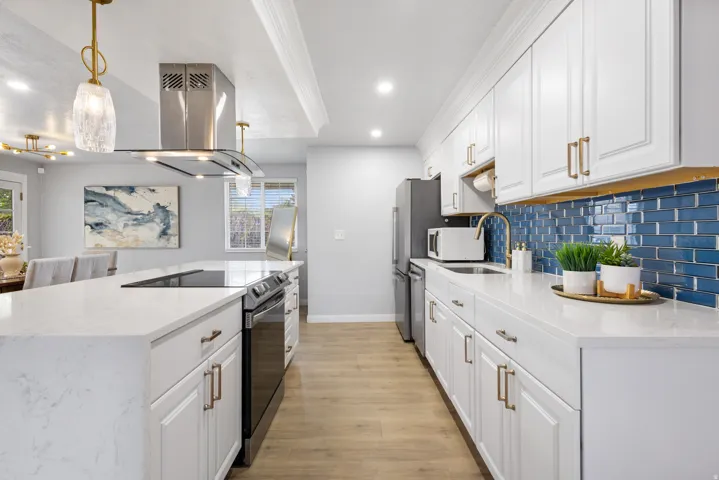 Kitchen featuring white shaker-style cabinetry, a blue subway tile backsplash, and light wood-finish flooring