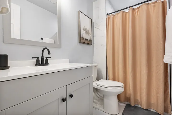Bathroom featuring a vanity with a white countertop and matte black faucet, framed mirror, and a shower with white tile surround