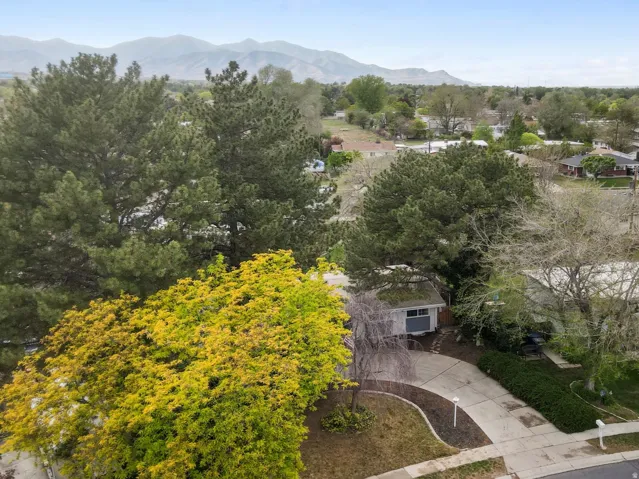 Aerial perspective showcasing a residential property with a curved driveway, mature trees, and a mountain range backdrop