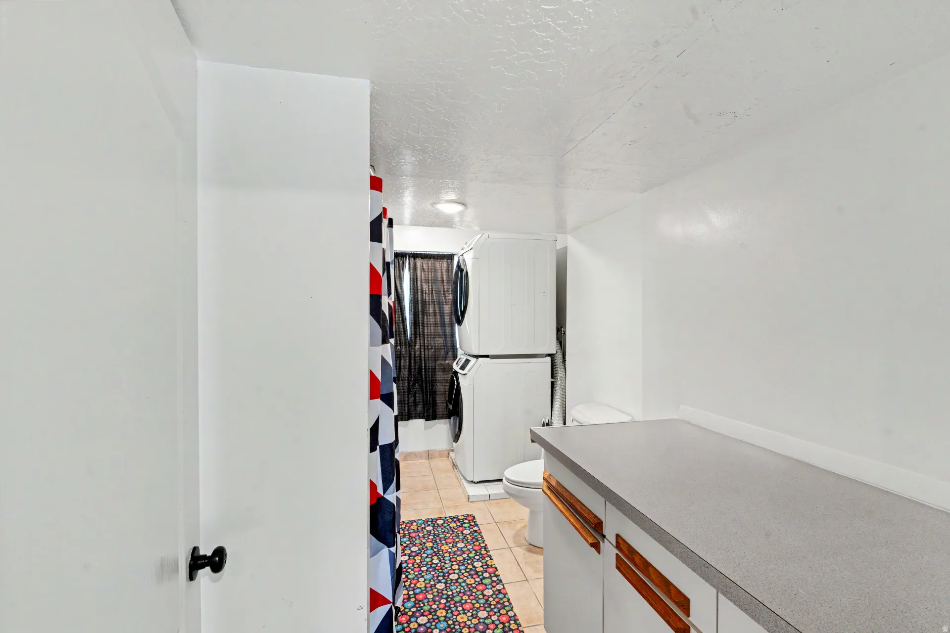 Laundry area featuring a stacked washer and dryer, tile flooring, and a built-in countertop with white cabinetry and wood-finish hardware