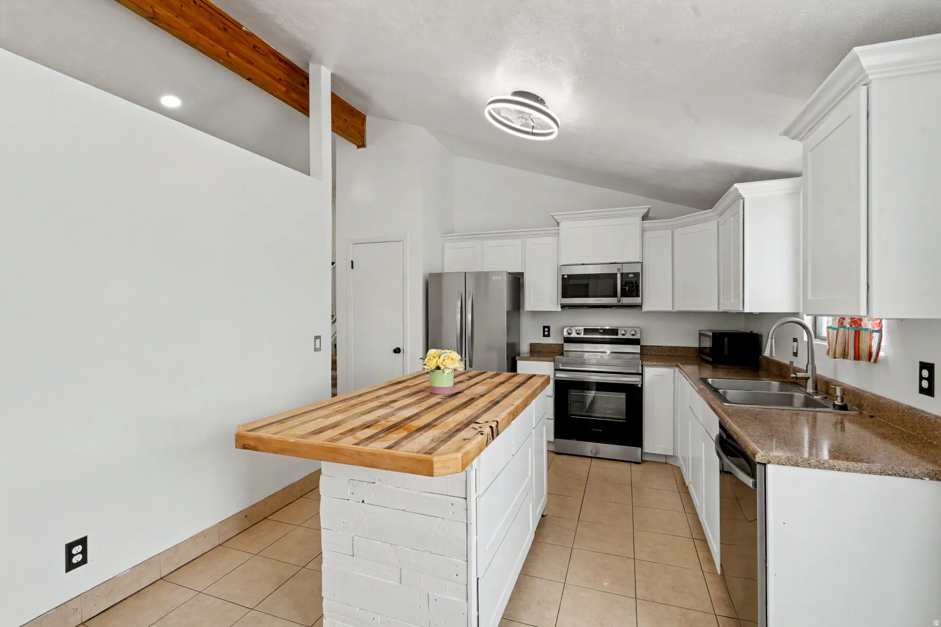 Kitchen featuring a wood-finish island, white cabinetry, stainless steel appliances, and a vaulted ceiling with exposed beams