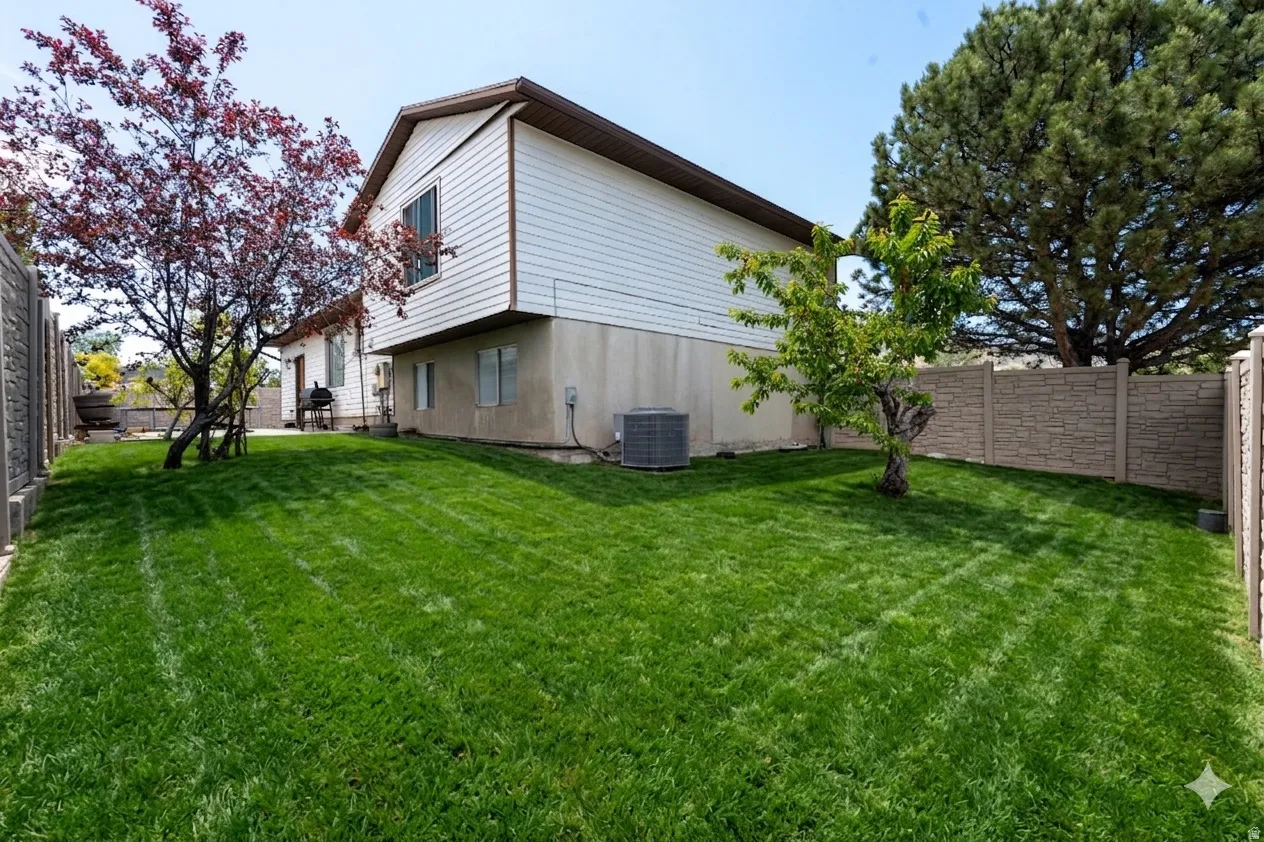 Expansive backyard featuring a lush lawn, established trees, and durable stone-look fencing