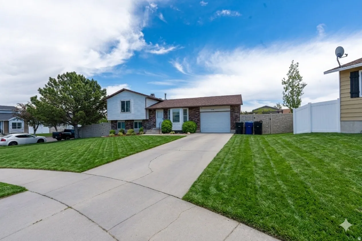 Ai enhanced front of this Split-level residence featuring a-car garage, concrete driveway, and a spacious front lawn with mature trees