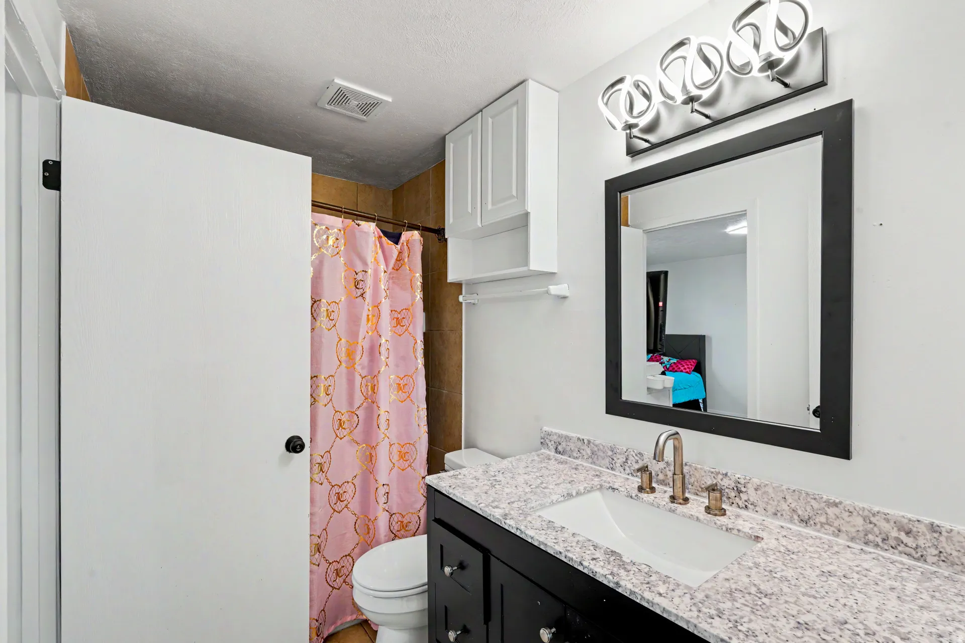 Bathroom featuring a vanity with dark cabinetry, integrated sink, and light speckled countertop