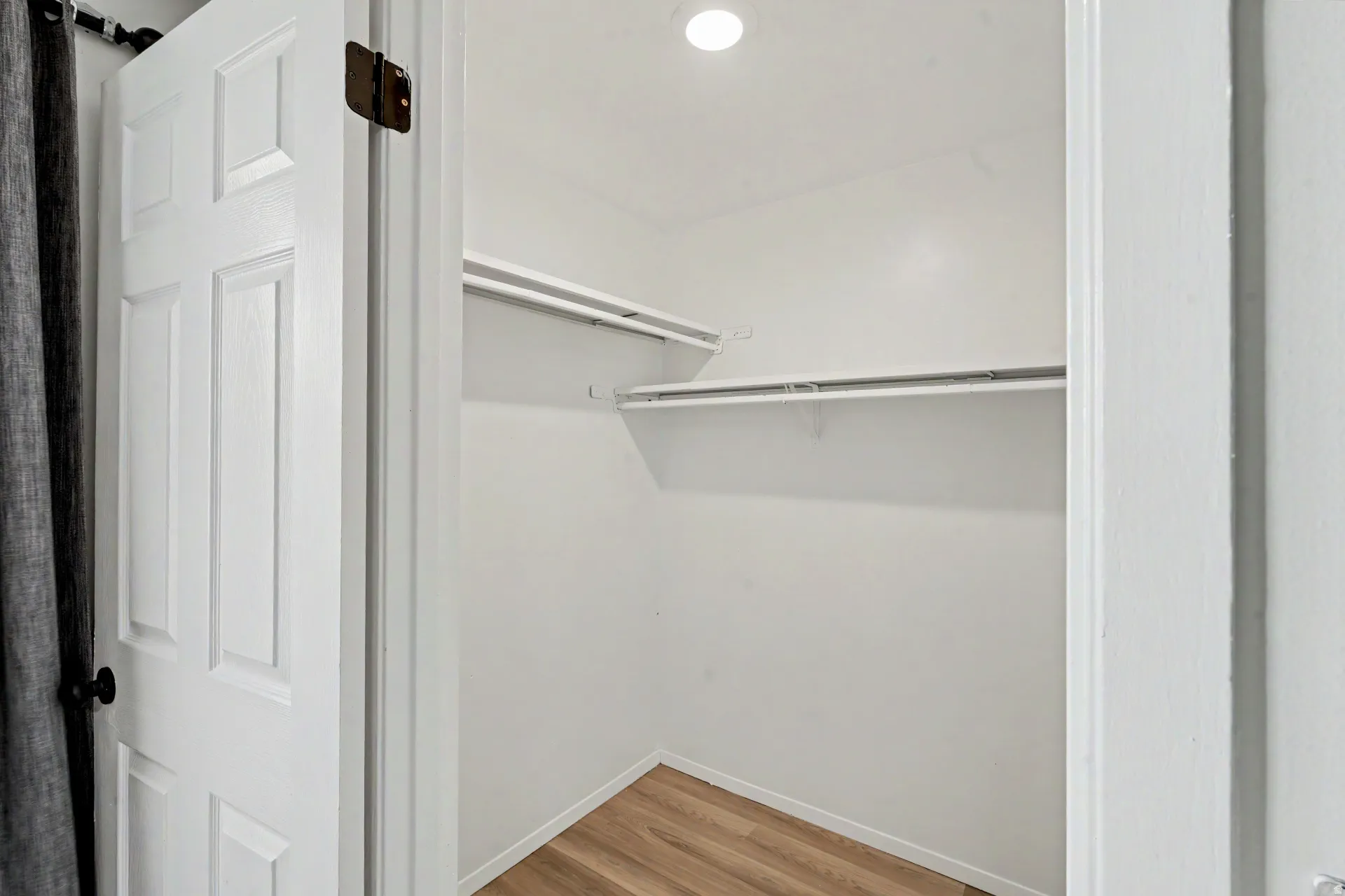 Closet with wood-finish flooring, white walls, and built-in shelving