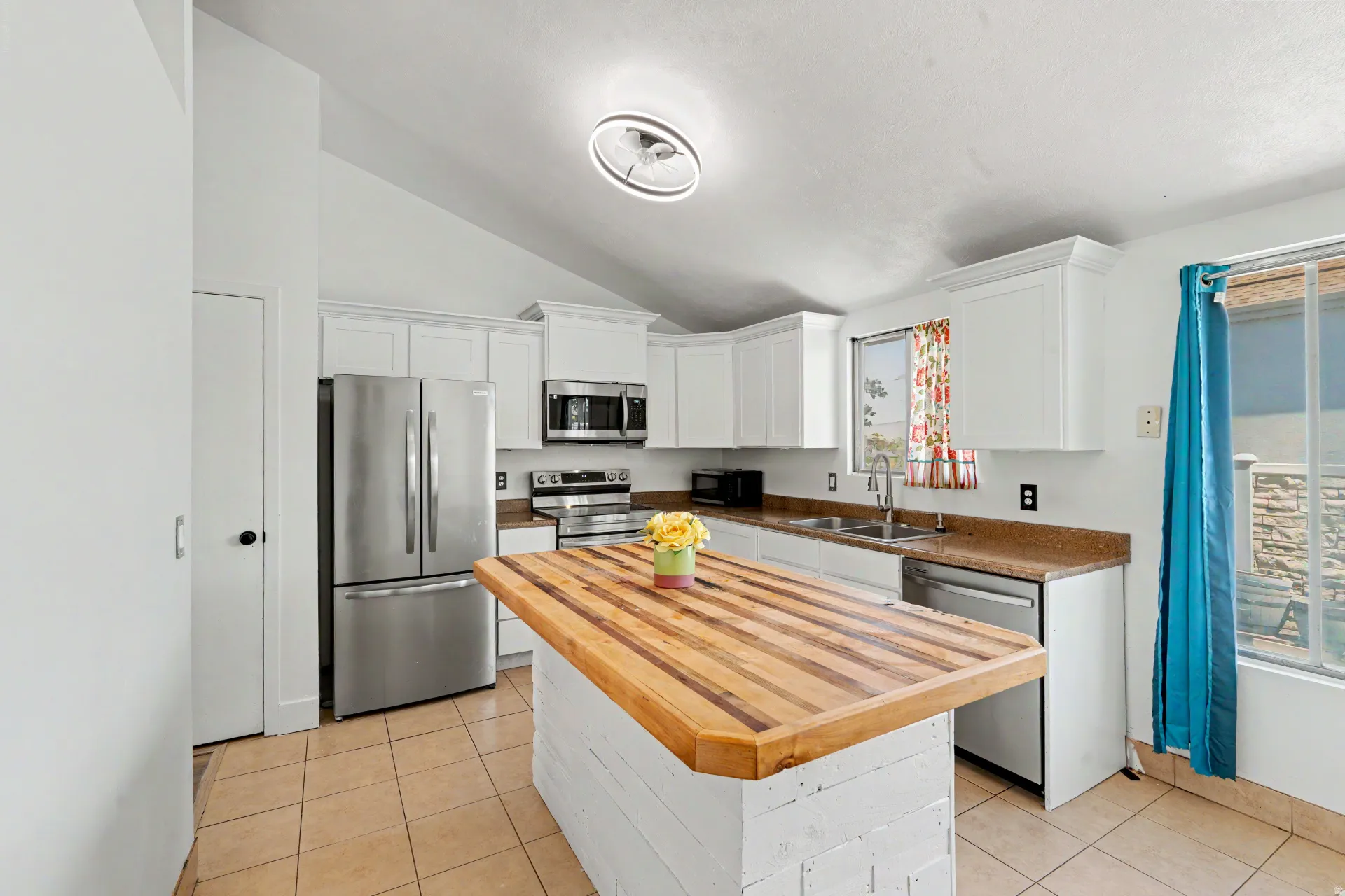 Kitchen featuring a custom wood-finish island, stainless steel appliances, white cabinetry, and light-toned tile flooring