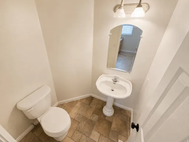 Powder room featuring a pedestal sink, white toilet, wall-mounted mirror, and tile flooring