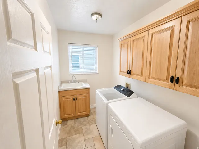 Dedicated laundry area featuring a utility sink, light wood cabinetry, and tiled flooring