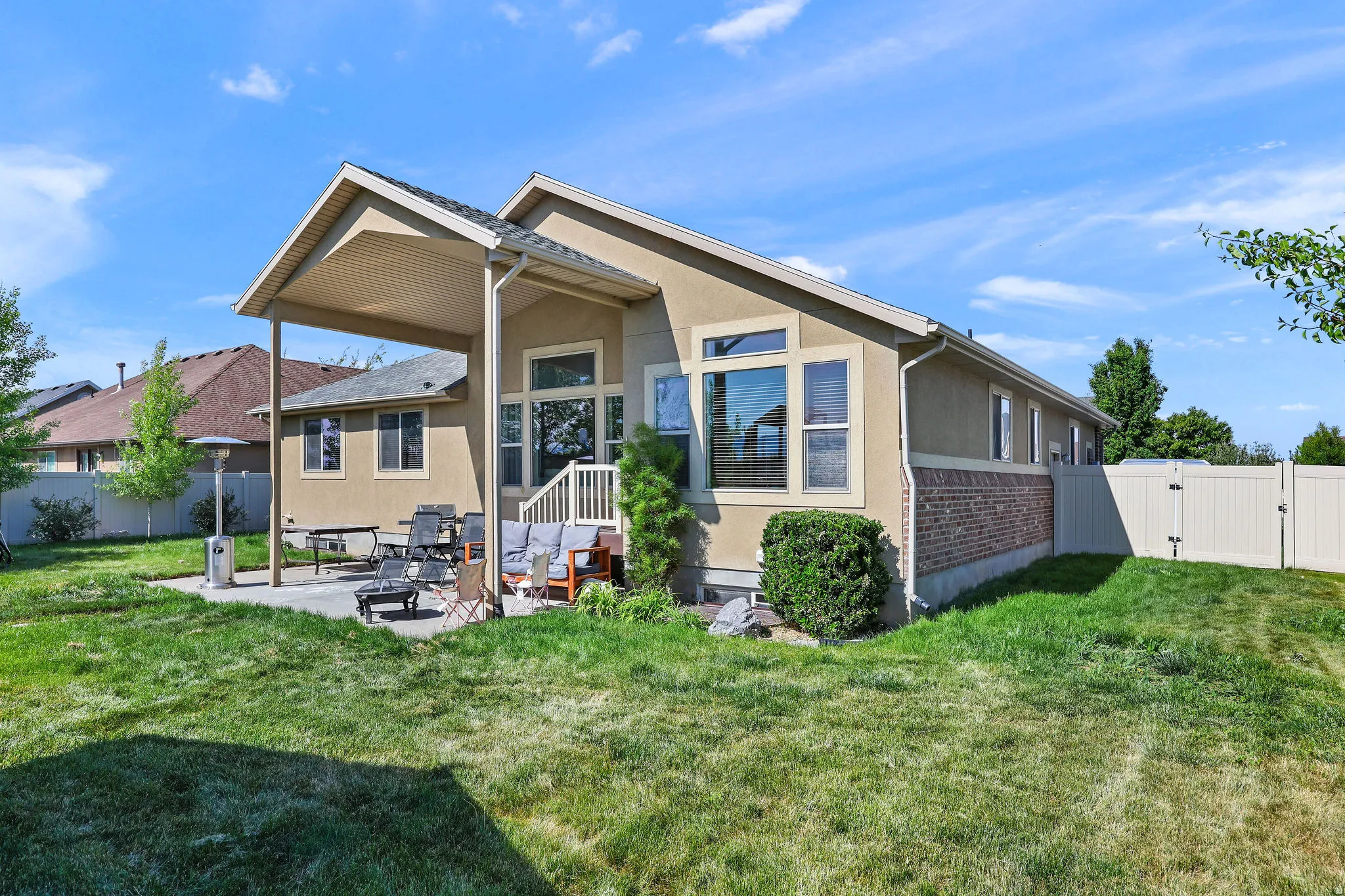 Rear exterior featuring a covered patio, brick foundation, stucco siding, and multiple windows